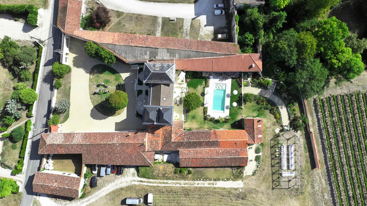 Aerial drone view of French rural estate with manor house, outbuildings, swimming pool, and vineyard rows