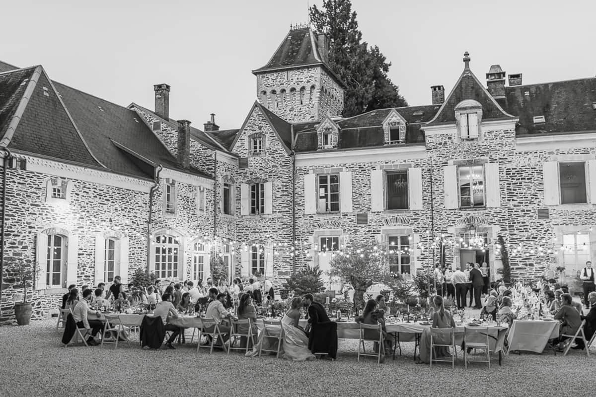 Black and white elevated view of chateau courtyard reception with 60-80 guests under string lights at evening