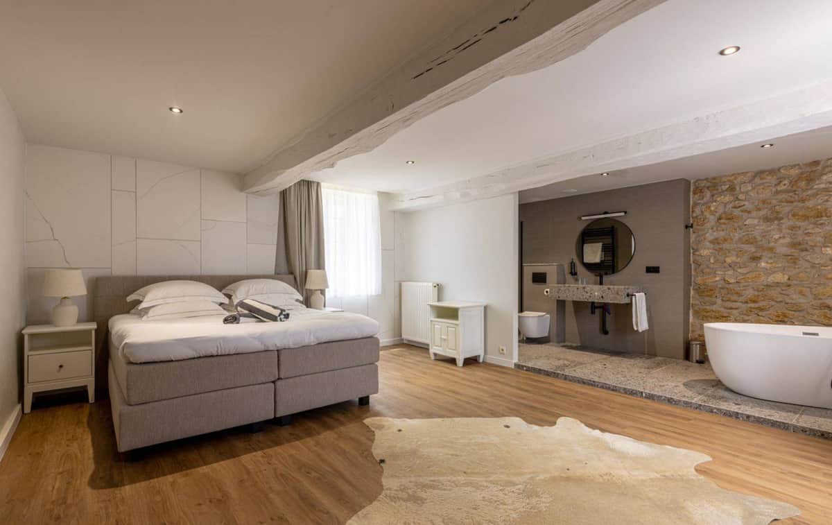 Hotel suite with king bed, cowhide rug, freestanding bathtub, and exposed stone wall in neutral tones