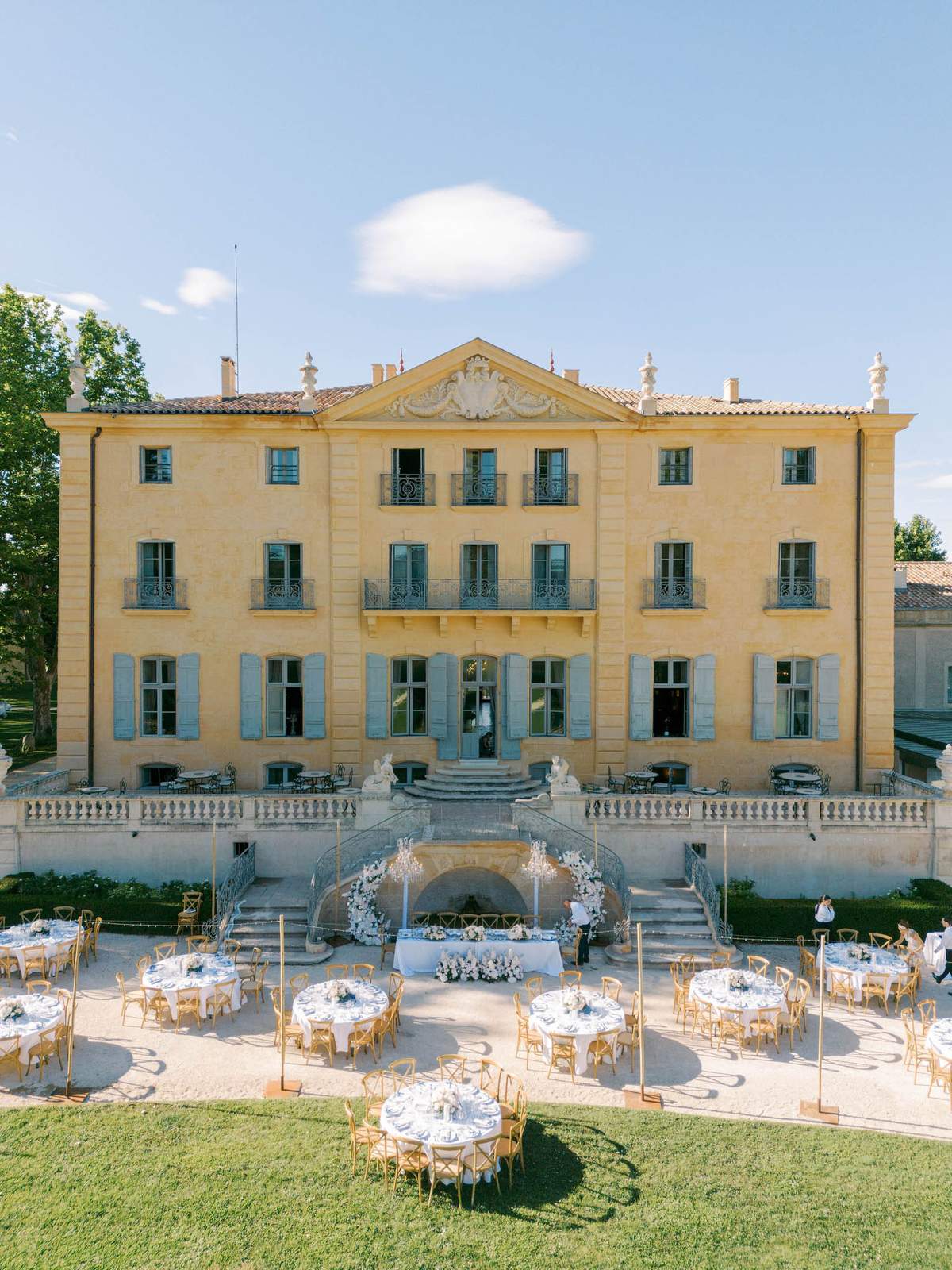 Aerial view of outdoor reception setup with round white tables and floral centerpieces on chateau forecourt