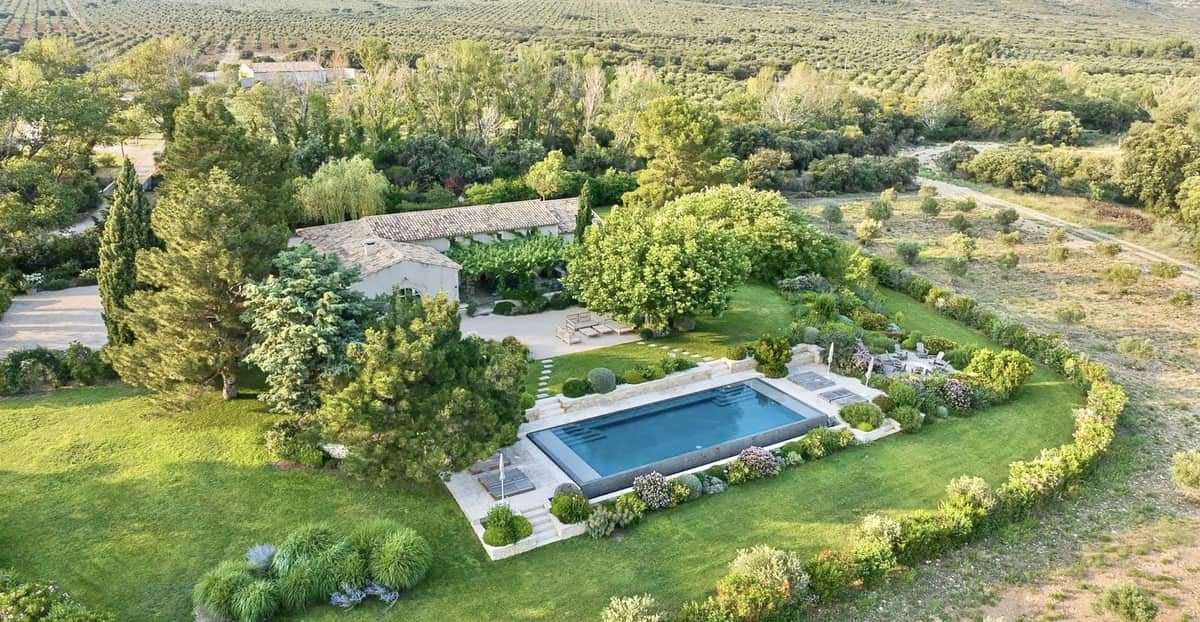 Aerial view of a Provencal stone farmhouse with pool, topiary gardens, and olive groves in open countryside