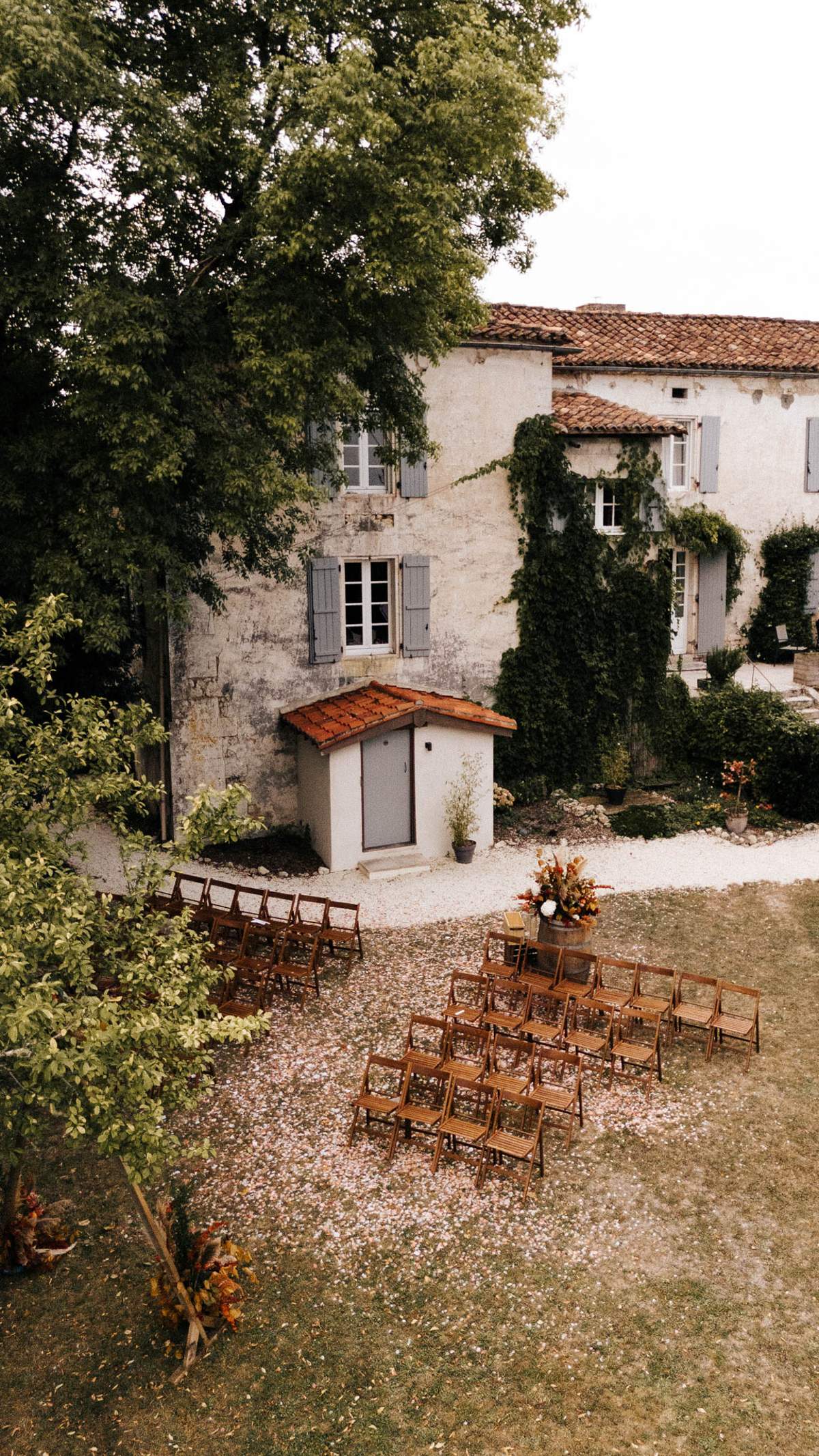 Aerial ceremony setup with pampas-topped barrel altar, rust floral aisle markers, and 30 chairs at stone manor