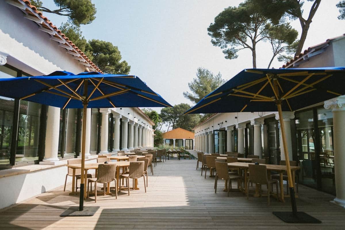 Courtyard dining terrace with blue parasols and pine trees at Domaine Rocabella, French Riviera