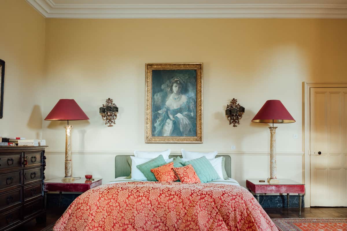 Chateau bedroom with red damask bedspread green headboard gilt portrait Persian rug and wrought iron chandelier