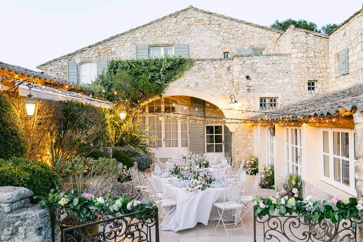 Outdoor reception setup in historic French stone courtyard with ivory linens and lavender centerpieces