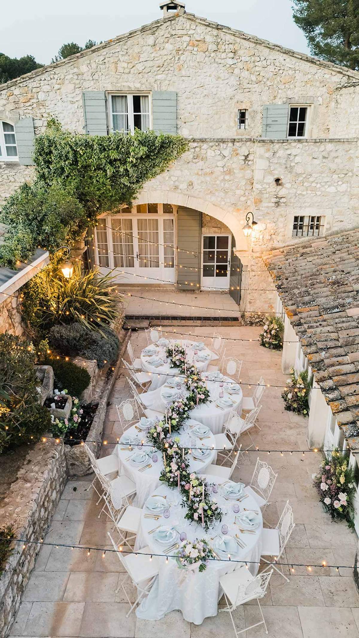 Aerial dusk view of four round reception tables with blush floral centrepieces and fairy lights in stone mas courtyard