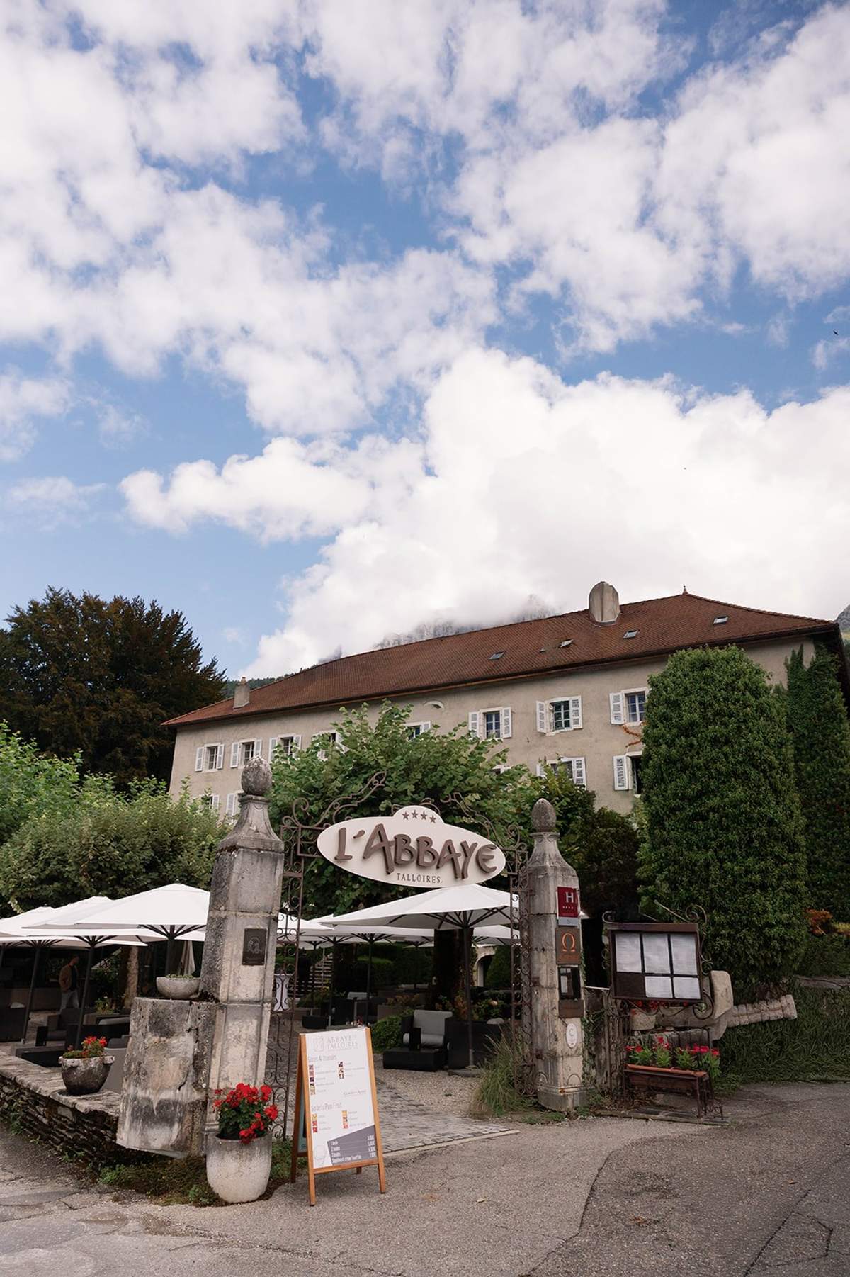 Stone gateway with L'Abbaye de Talloires sign beneath Alpine cloud at Abbaye de Talloires