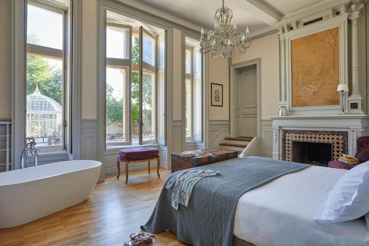 Chateau bedroom with freestanding soaking tub, marble fireplace, crystal chandelier, and French windows
