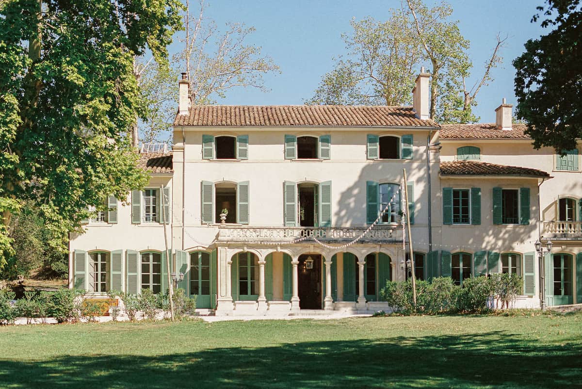 Provencal manor house with cream facades, terracotta roof, sage green shutters, and arched colonnade entrance
