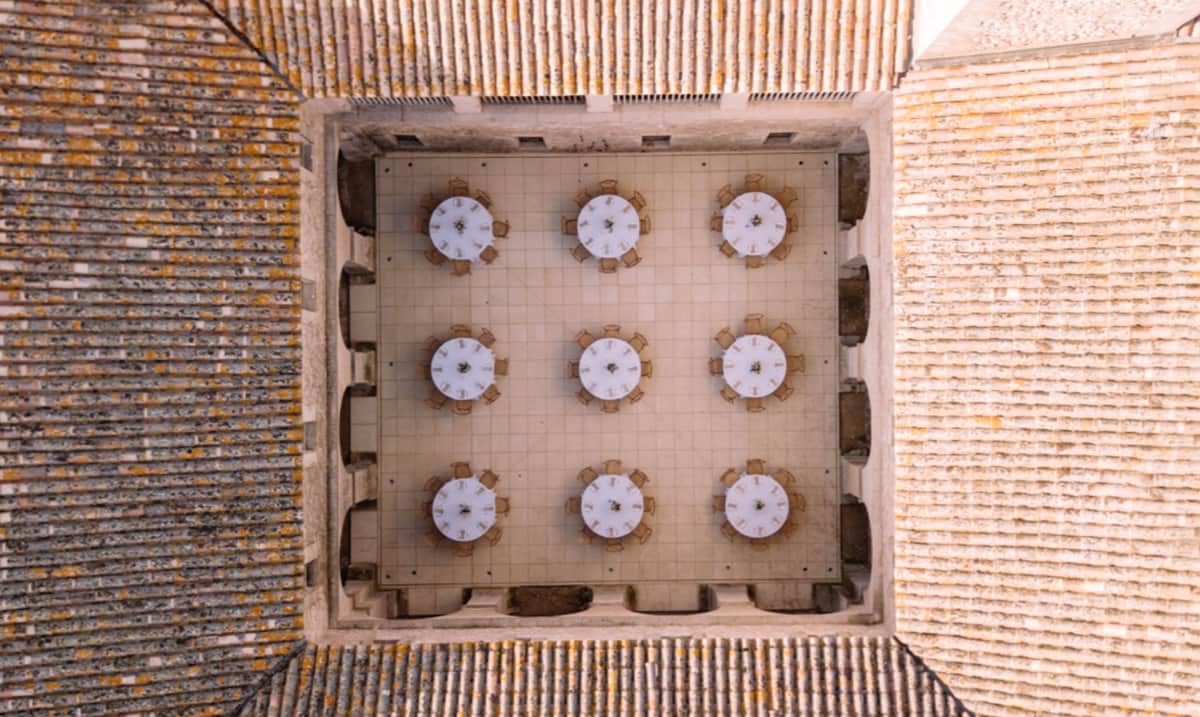 Aerial view of nine round tables in stone courtyard with terracotta roofs and arched recesses