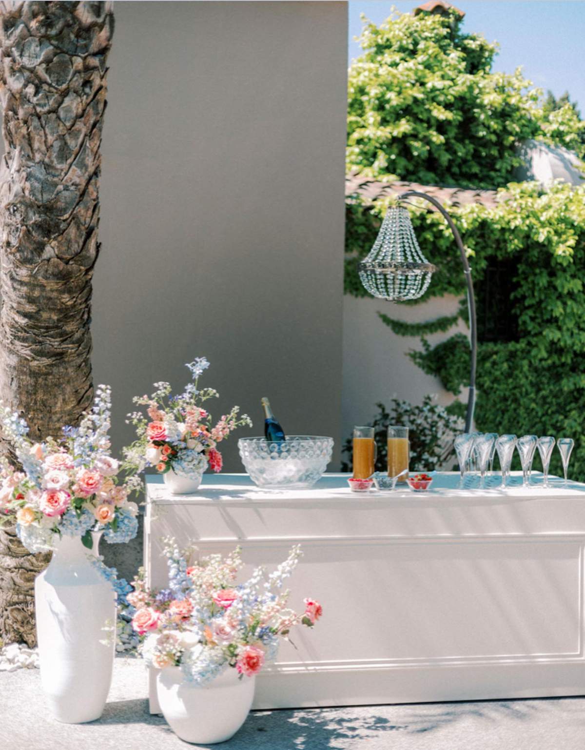Outdoor cocktail bar with champagne flutes, punch bowl, and peach roses with blue hydrangea arrangements