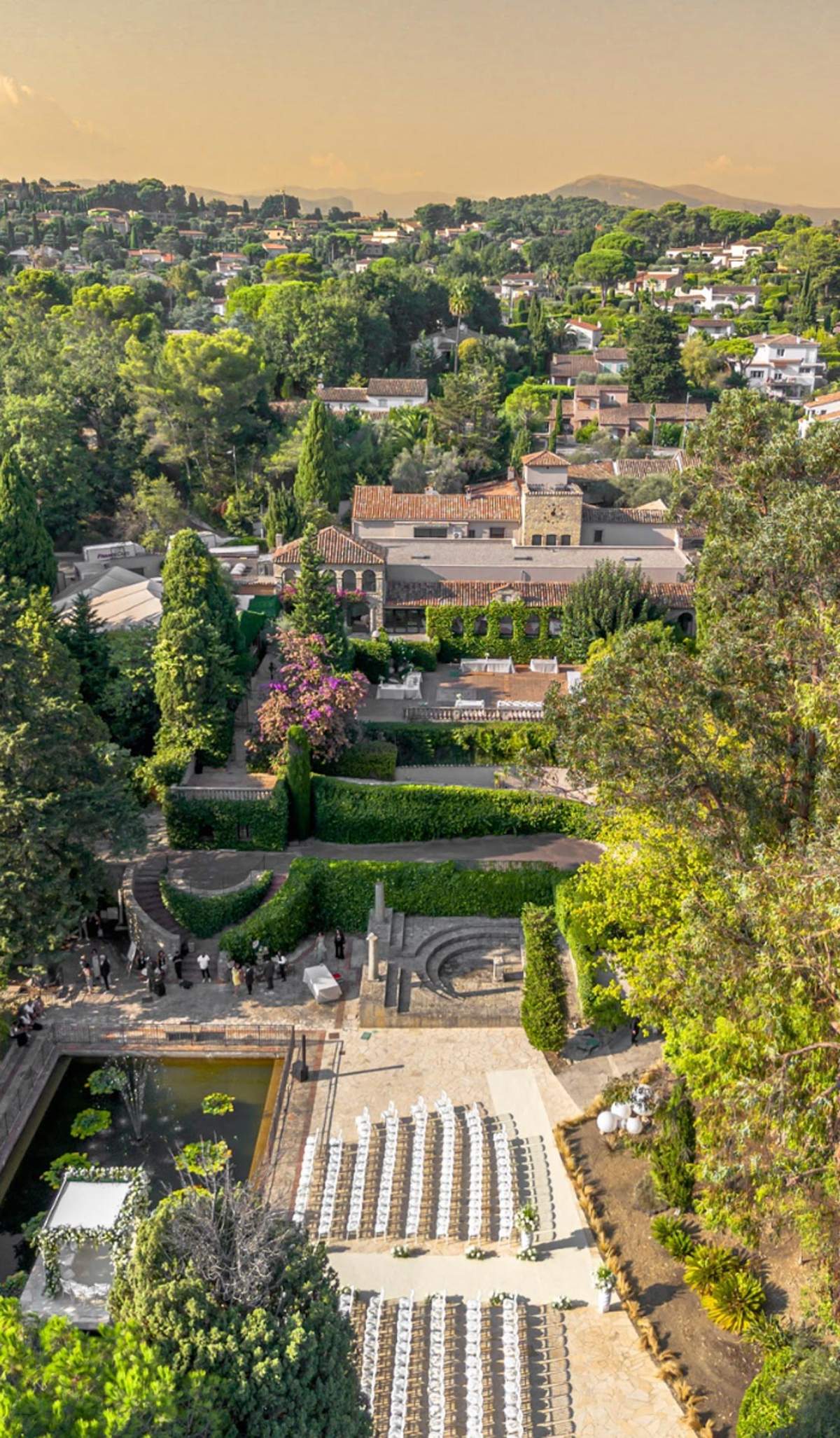 Aerial golden hour view of Provencal estate with ceremony seating, parterre gardens, and clock tower