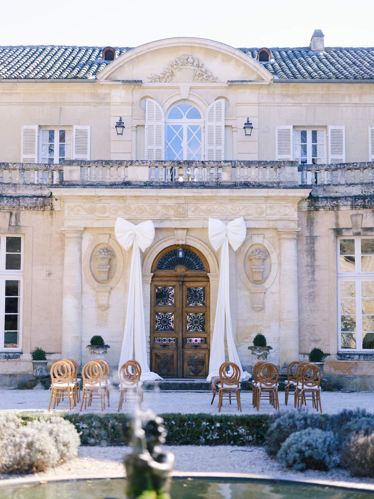 Neoclassical château facade with two oversized ivory satin bows over carved wood door and ceremony chairs