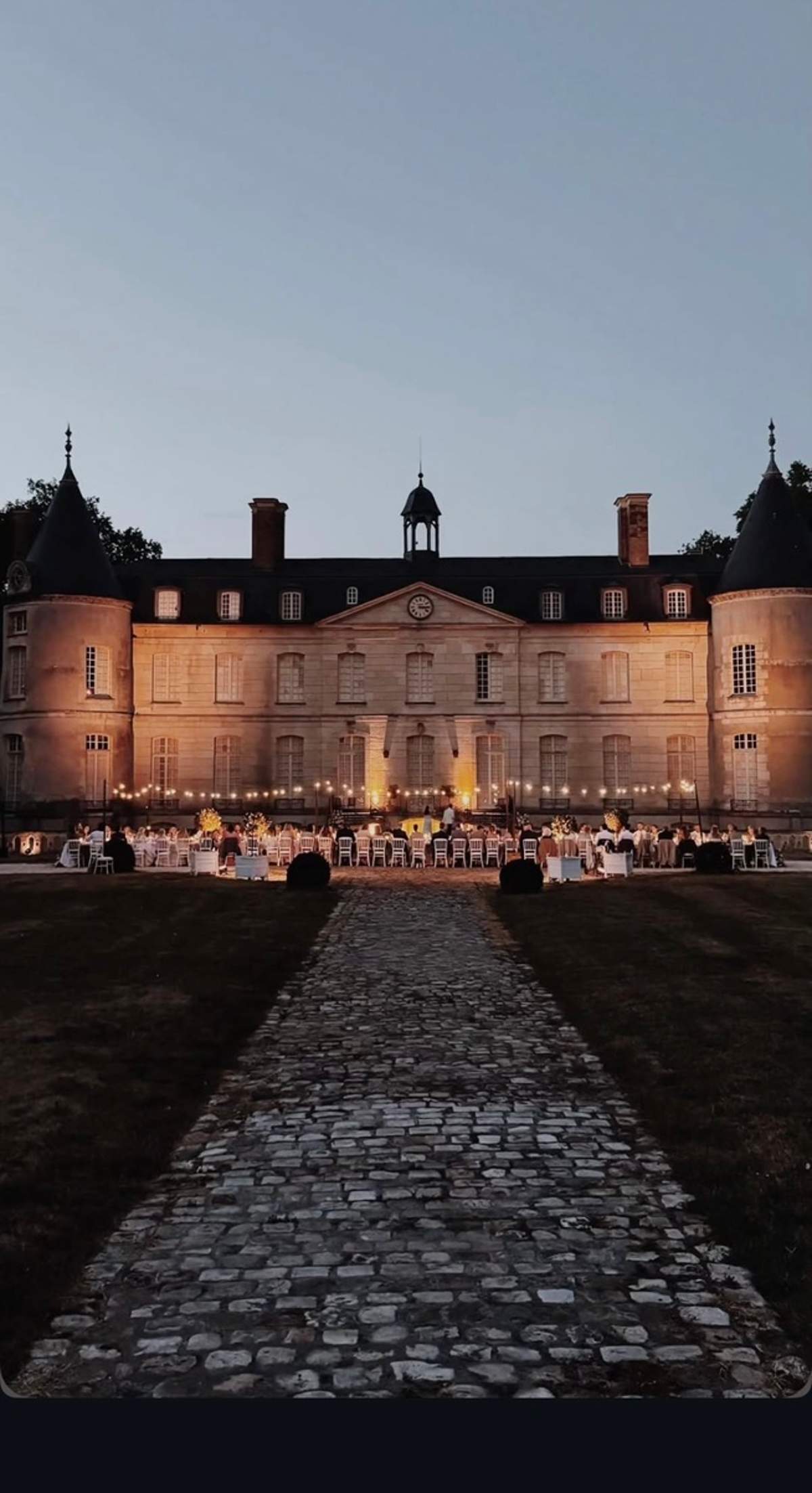 Evening wedding reception dinner in front of the château at Domaine de Verderonne, guests seated under string lighting.
