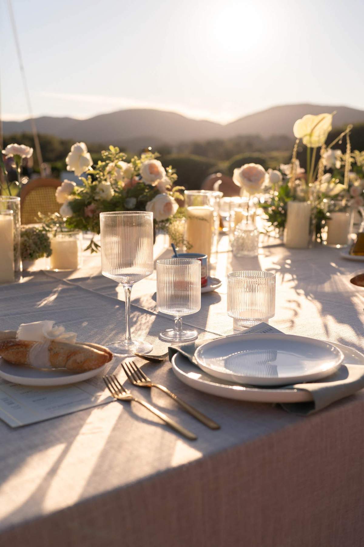 Sunset wedding dinner table with white roses, candles and ribbed glassware, designed by Agence Fairytale