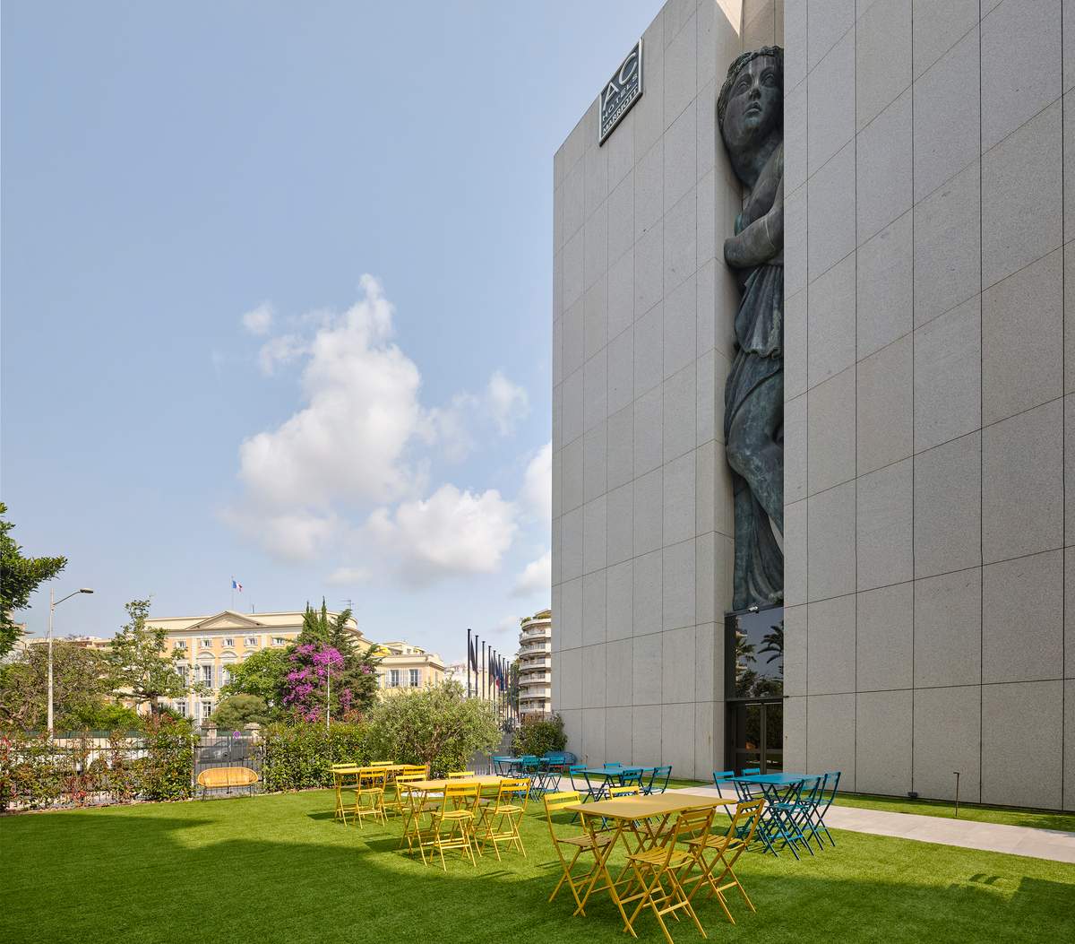 Garden of Montcalm Nice with yellow and blue bistro tables beside the hotel façade and its Venus sculpture