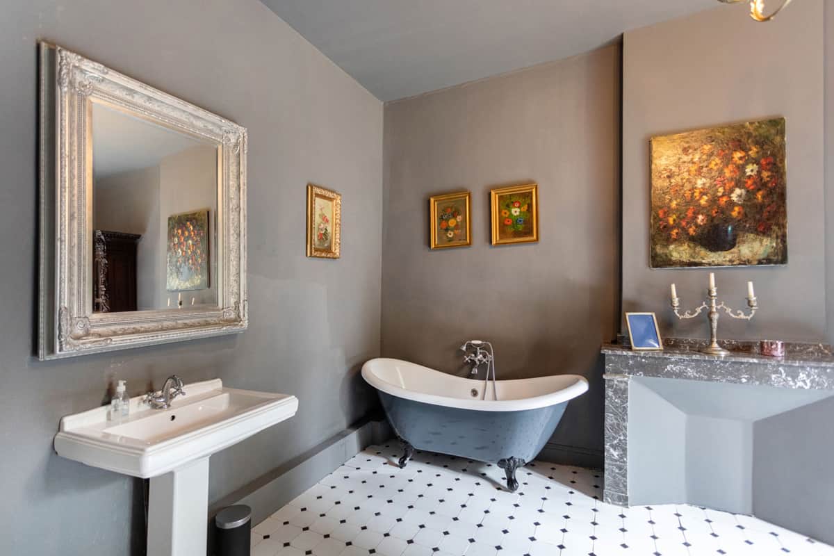 An ensuite bathroom with a clawfoot bathtub, marble fireplace and framed artwork.