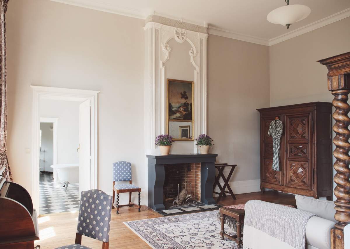 Bedroom with a grey fireplace, lavender pots, a carved wardrobe and a roll-top bath visible through the doorway