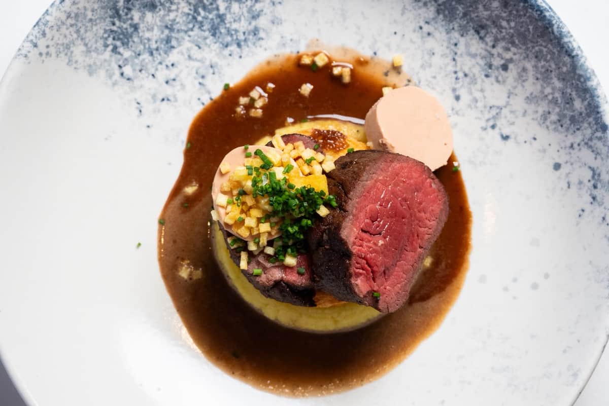 Seared beef fillet with foie gras on a potato base, finished with jus and chives, seen from above