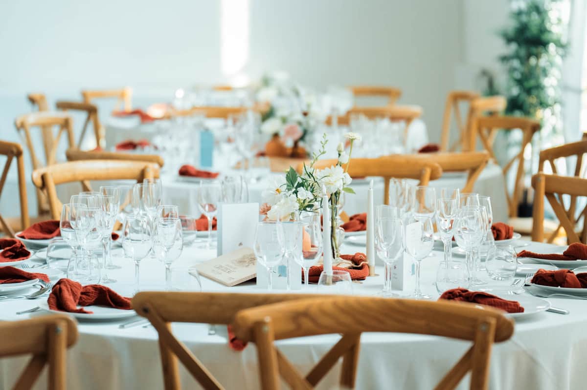 Close-up of a round dining table in the Orangery Hall with terracotta napkins, ivory florals, candles and menu cards