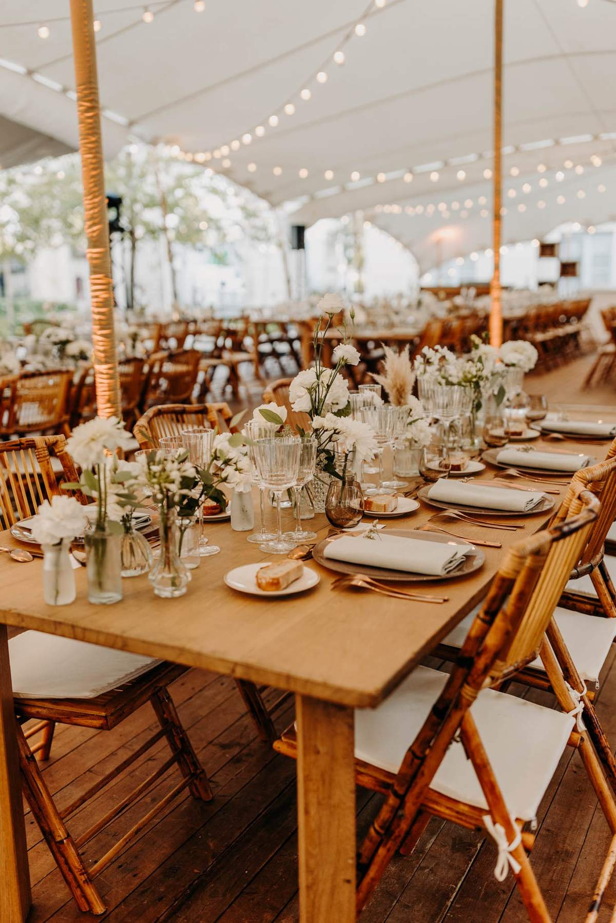 Stretch tent dining at Chateau de l'Hospital with wooden tables, floral runners and amber glassware