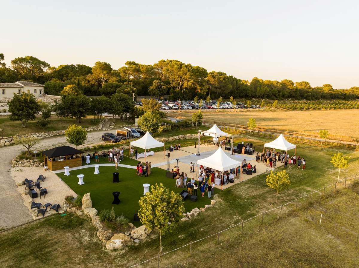 Aerial view at dusk of the Garden Feerie lawn with white pavilion tents, cocktail tables and a stage.