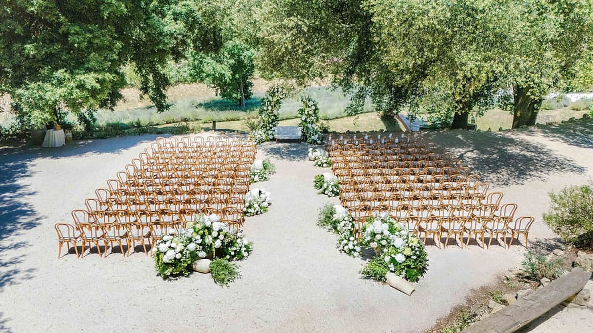 Aerial view of outdoor wedding ceremony with floral arch and wooden chairs at Domaine de Valbonne