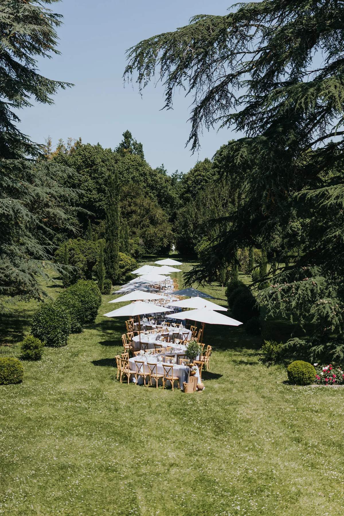 Long table dinner under white parasols on the lawn, seen from above