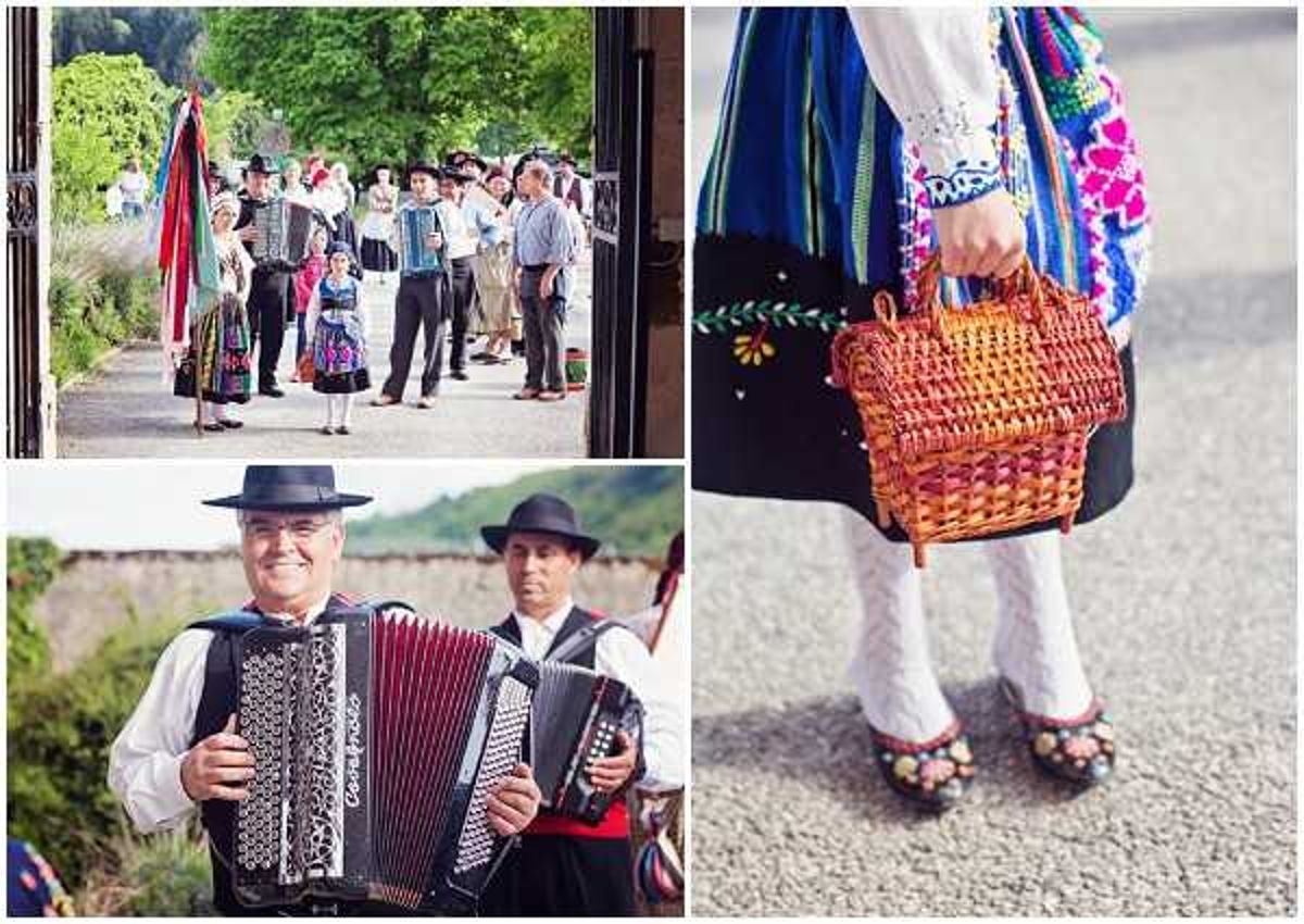A three-image collage documenting a traditional folk wedding procession and musicians. The top-left wide shot shows a group of approximately 15-20 guests and participants walking along a tree-lined path in traditional regional folk costumes, including embroidered blouses, colorful patterned skirts, and black hats, with decorative ribboned poles or flags visible. The bottom-left portrait shows two men in traditional dress — white shirts, black vests, and black wide-brimmed hats — playing accordions outdoors, with a lake or river visible in the background. The right detail shot is a close-up of a child or woman's lower half wearing a vibrant embroidered and multi-colored folk costume, white lace tights, black embroidered shoes with floral accents, and carrying a woven wicker basket with floral detailing. The styling throughout reflects Central or Eastern European folk wedding traditions with richly embroidered textiles, bold colors including red, blue, green, and black, and handcrafted accessories.