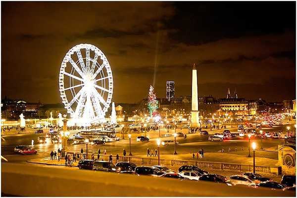 This image does not appear to be a wedding photograph. It is a nighttime cityscape shot of the Place de la Concorde in Paris, featuring a large illuminated Ferris wheel, the Luxor Obelisk, a lit Christmas tree, street lamps, vehicle traffic, and pedestrians. The wide shot captures the full plaza with warm amber artificial lighting against a dark evening sky. There are no wedding-related subjects, people, or events visible in this image.