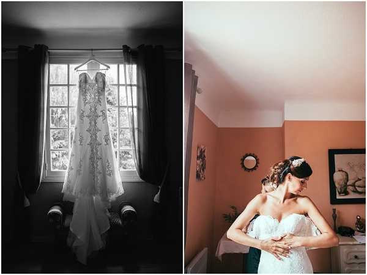 A two-image composite showing bridal preparations. The left image is black-and-white, featuring a lace-detailed wedding gown hanging on a hanger in front of a multi-pane window, with dark curtains framing the sides and an armchair visible below; the high contrast lighting silhouettes the room while the window backlights the dress, highlighting its lace appliqué and cathedral-length train. The right image, shot in color, shows the bride in a strapless, lace-bodiced white gown being helped into or adjusted by an assistant in a terracotta-walled room furnished with a white dresser, a circular mirror, and a framed artwork; the bride's dark hair is styled up with a decorative floral hairpiece. Both shots are portrait-style, close to medium distance, documenting the getting-ready phase of the wedding day.