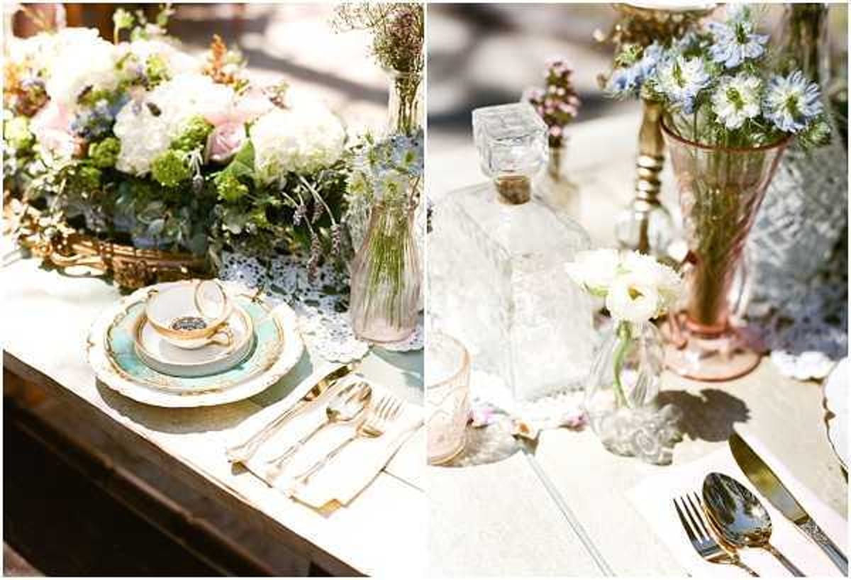 Close-up detail shot of a vintage-styled outdoor wedding tablescape, shown as a split diptych. The left image features mismatched vintage china in pale aqua and white with gold rims, stacked as a place setting with gold flatware and a white linen napkin, alongside a lush centerpiece of white hydrangeas, blush roses, green foliage, and wildflowers arranged in a gold basket, set on a white doily runner. The right image shows a collection of vintage glassware including a faceted crystal decanter, pink Depression glass vases, and small bud vases holding white ranunculus and blue nigella flowers, also on a doily runner with silver flatware. The overall styling theme is vintage/antique with a soft palette of blush, aqua, white, and gold, incorporating mismatched collectible pieces for a tea-party-inspired aesthetic.
