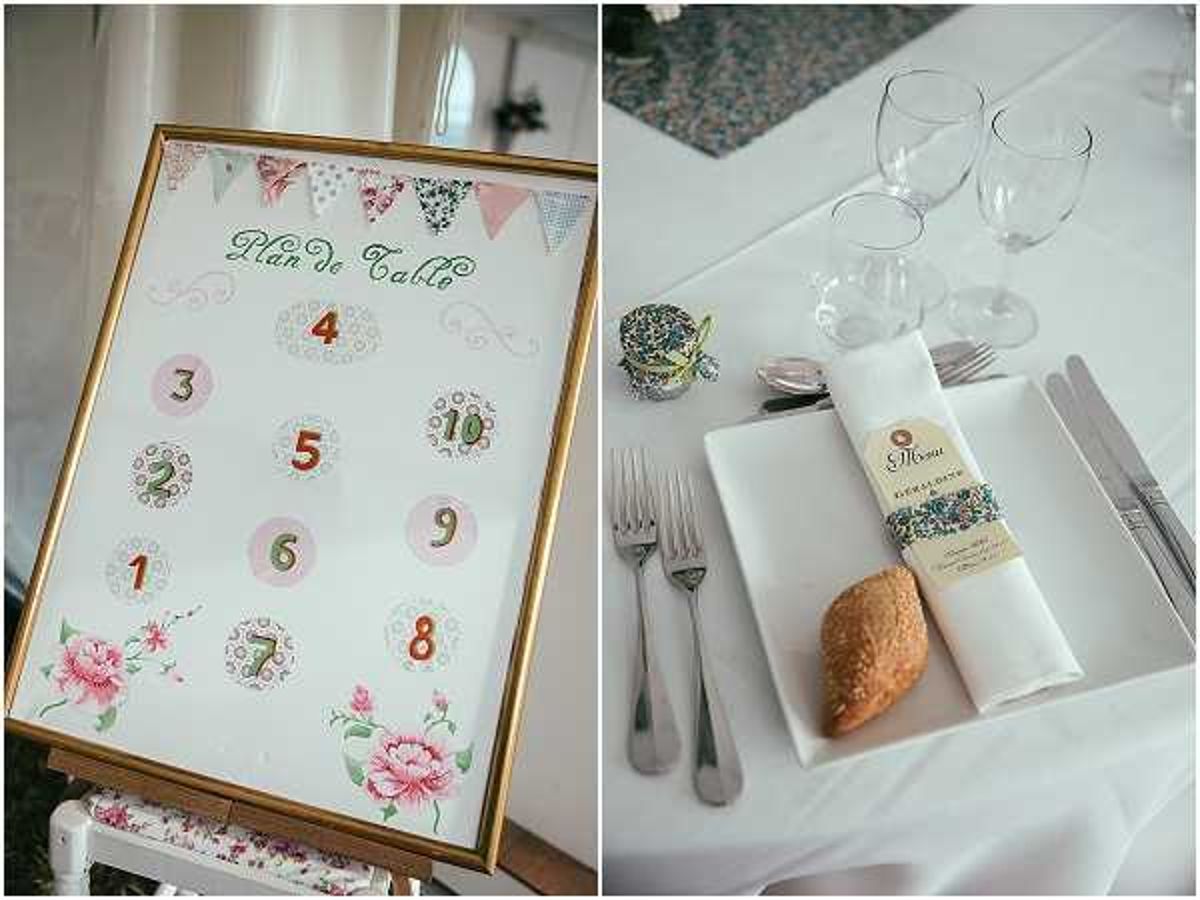 A split image showing two reception detail shots from a French wedding. On the left, a gold-framed seating chart labeled 'Plan de Table' in green script displays table numbers 2 through 10 in colorful pastel circles, decorated with pink floral illustrations and a bunting banner graphic at the top, displayed on a floral-printed easel. On the right, a close-up of a place setting on a white tablecloth shows a folded white napkin wrapped with a Liberty-print floral band and a printed menu card, a small bread roll on top, flanked by silver forks and a knife, with clear wine glasses in the background. The overall styling theme is vintage and whimsical with a Liberty/floral print palette of pinks, greens, and soft pastels. Both shots are detail close-ups.