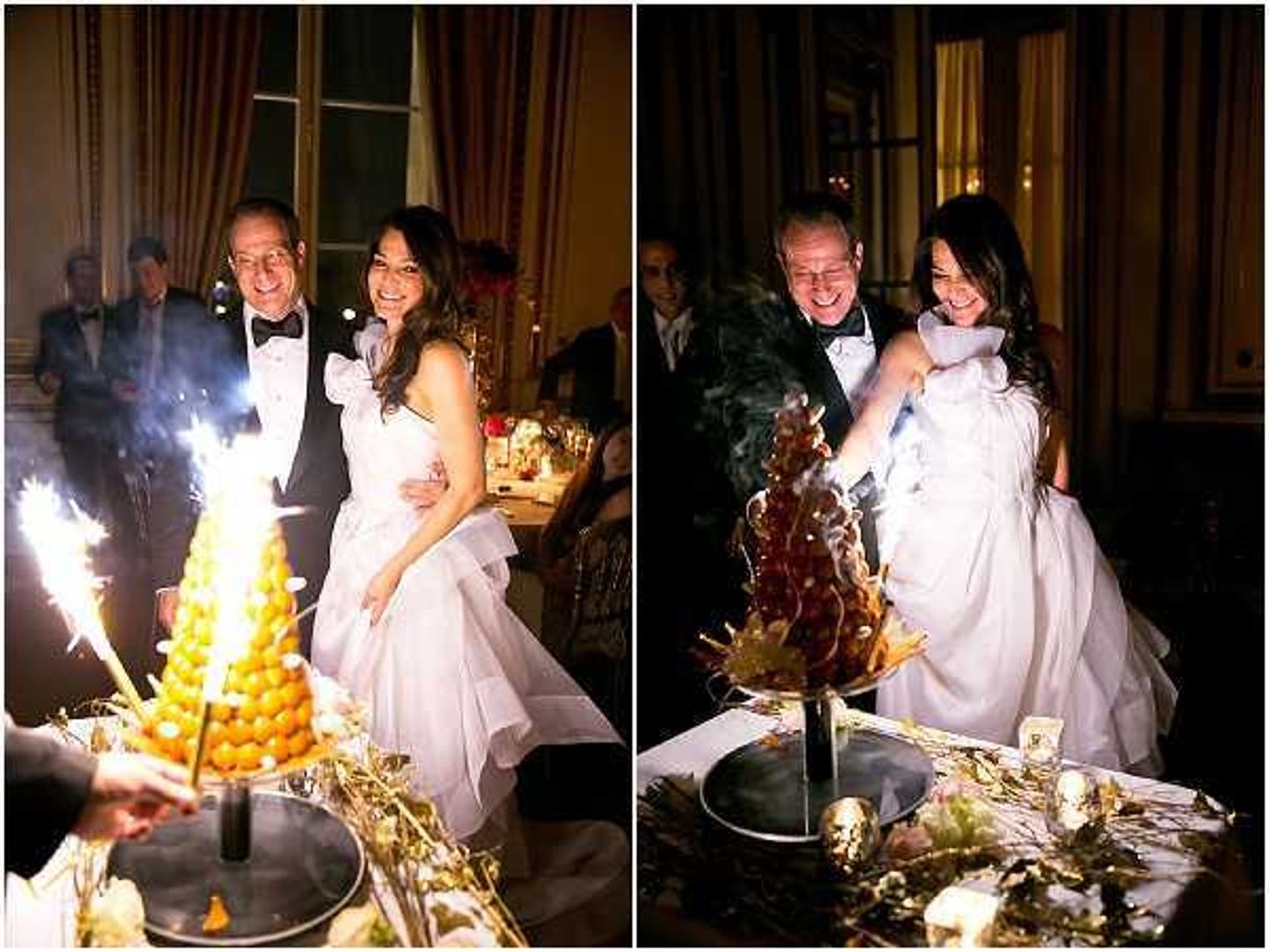 A two-panel image capturing a cake cutting moment at an indoor evening reception, set in what appears to be a formal chateau or grand salon with warm amber lighting. The bride wears a white strapless ballgown with a ruffled skirt, and the groom is dressed in a black tuxedo with bow tie. In the left panel, the couple stands smiling beside a traditional French croquembouche — a tower of choux puffs — decorated with gold accents and lit sparklers placed around its base on a silver tray. In the right panel, the bride is actively cutting into the croquembouche, now smoking from the extinguished sparklers, with caramelized profiteroles visible in the structure. The table displays gold leaf decorative elements and small votive candles, with other formally dressed guests visible in the dimly lit background. Both panels are close-to-medium portrait shots with warm, low-light reception ambiance.
