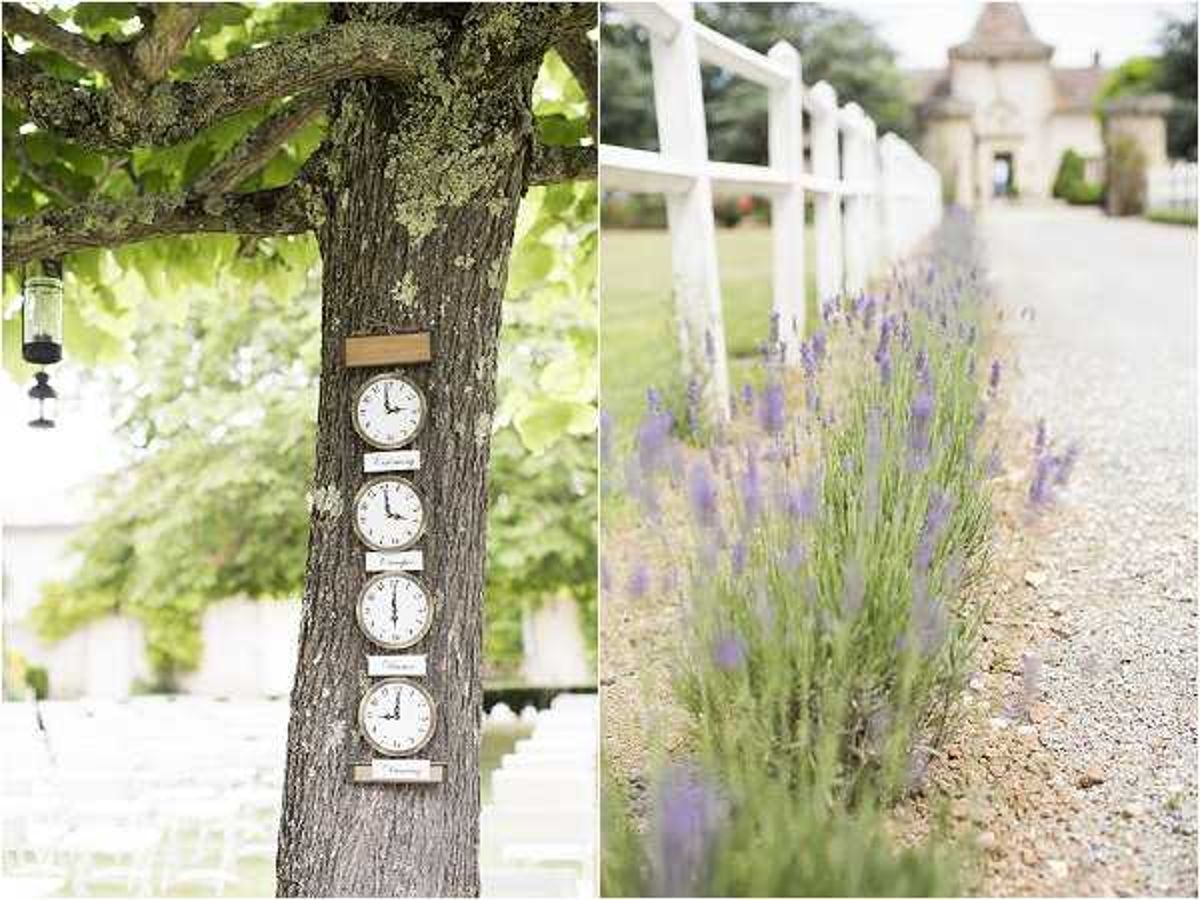 A two-image composite showing outdoor wedding venue details. On the left, four clocks mounted vertically on a tree trunk display different time zones, likely representing locations meaningful to the couple, with white ceremony chairs visible in the background beneath the tree and a small hanging lantern to the left. On the right, a gravel driveway lined with rows of purple lavender plants leads toward a white fence and a stone château gatehouse in the soft-focus background. Both shots are close-up detail images with a light, airy exposure. Potential venue feature image.