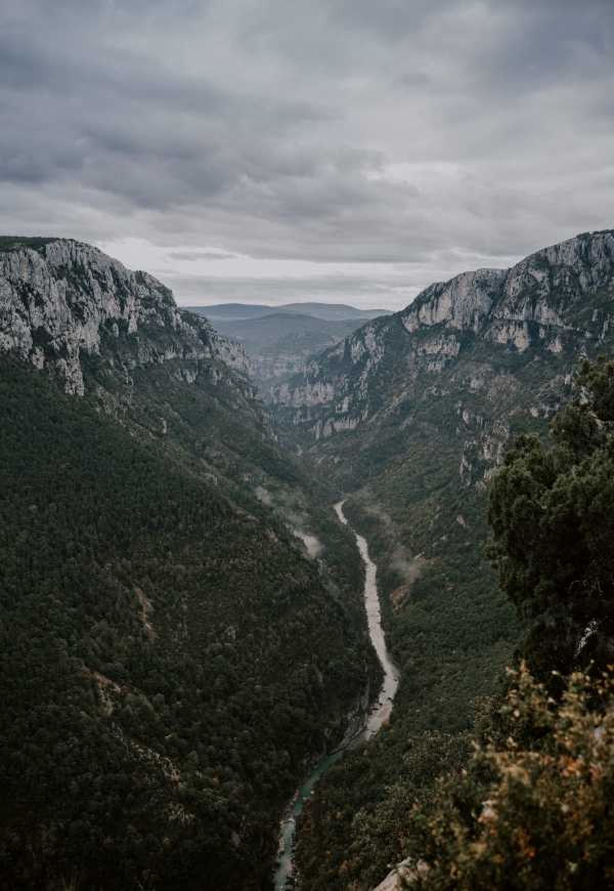 This image contains no people, wedding activity, or intentional design elements associated with a wedding. It is a wide landscape shot of a deep river gorge — likely the Gorges du Verdon in southern France — viewed from a high vantage point, with a narrow river winding through the valley floor far below. No couple, bridal party, decor, florals, or wedding-related subjects are visible in the frame.