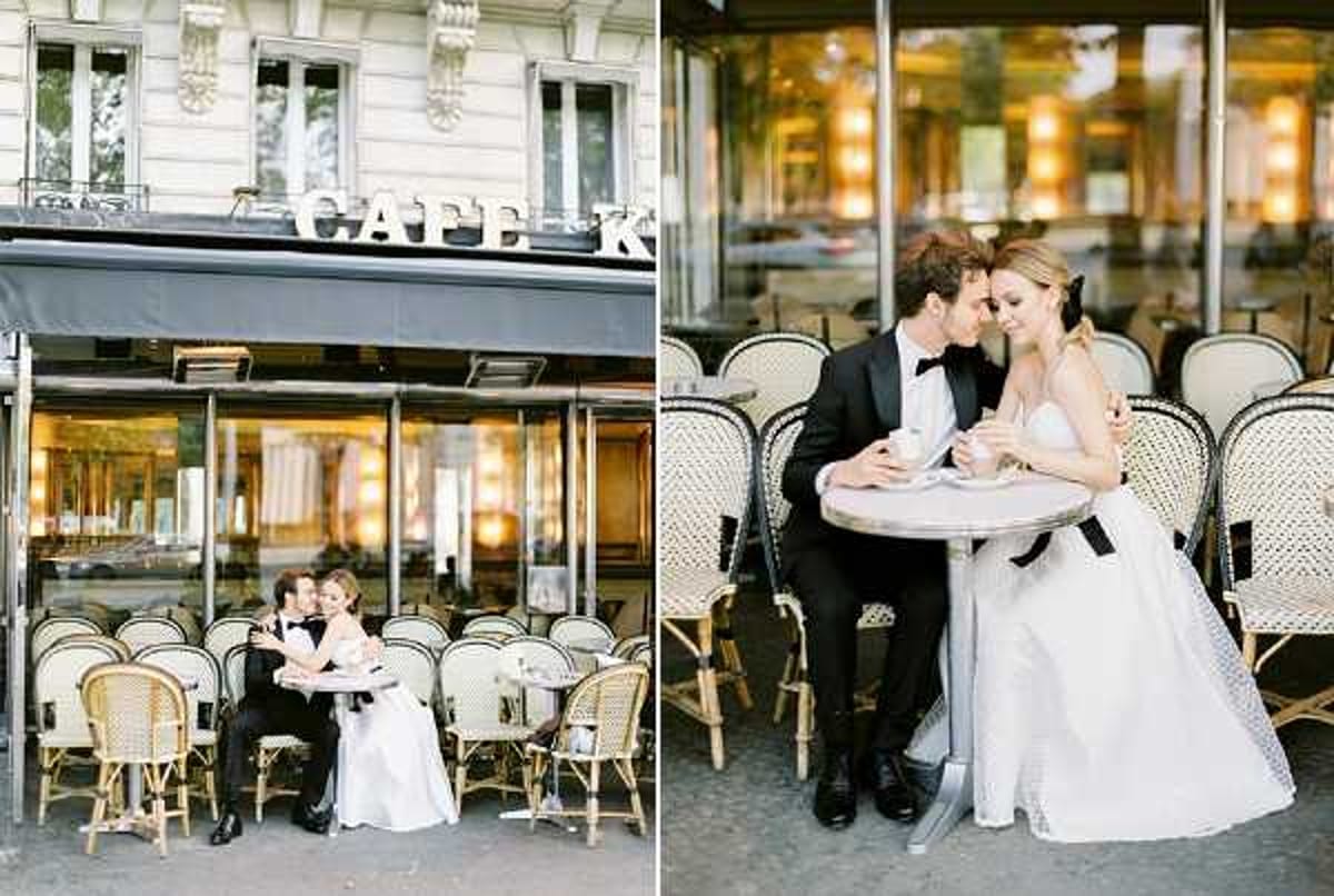 A couple in wedding attire poses at a classic Parisian café terrace, shown in two companion shots — one wide and one closer portrait. The groom wears a black tuxedo with bow tie, and the bride wears a strapless white ballgown with a full skirt. They are seated at a small round bistro table surrounded by traditional rattan café chairs. The café signage reading 'Café K' is visible in the wider left shot, with a Haussmann-style building facade in the background. In the closer right shot, the couple leans toward each other intimately with espresso cups on the table, and warm amber lighting glows through the café window behind them. The styling is classic and Parisian in tone, with a clean black-and-white color palette in the couple's attire.