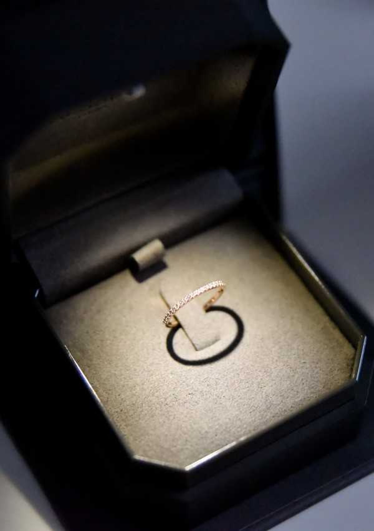 Close-up detail shot of a rose gold eternity band set with small pavé diamonds, displayed upright in an open black jewelry box with a cream velvet interior. The ring is slim and delicate, fully encircled with stones, and is spotlit against the pale cushioned lining, casting a circular shadow. The box has a dark lacquered octagonal exterior with a black satin lid lining. No people are visible; this is a ring detail image likely taken during the getting-ready or flat-lay portion of the wedding day.