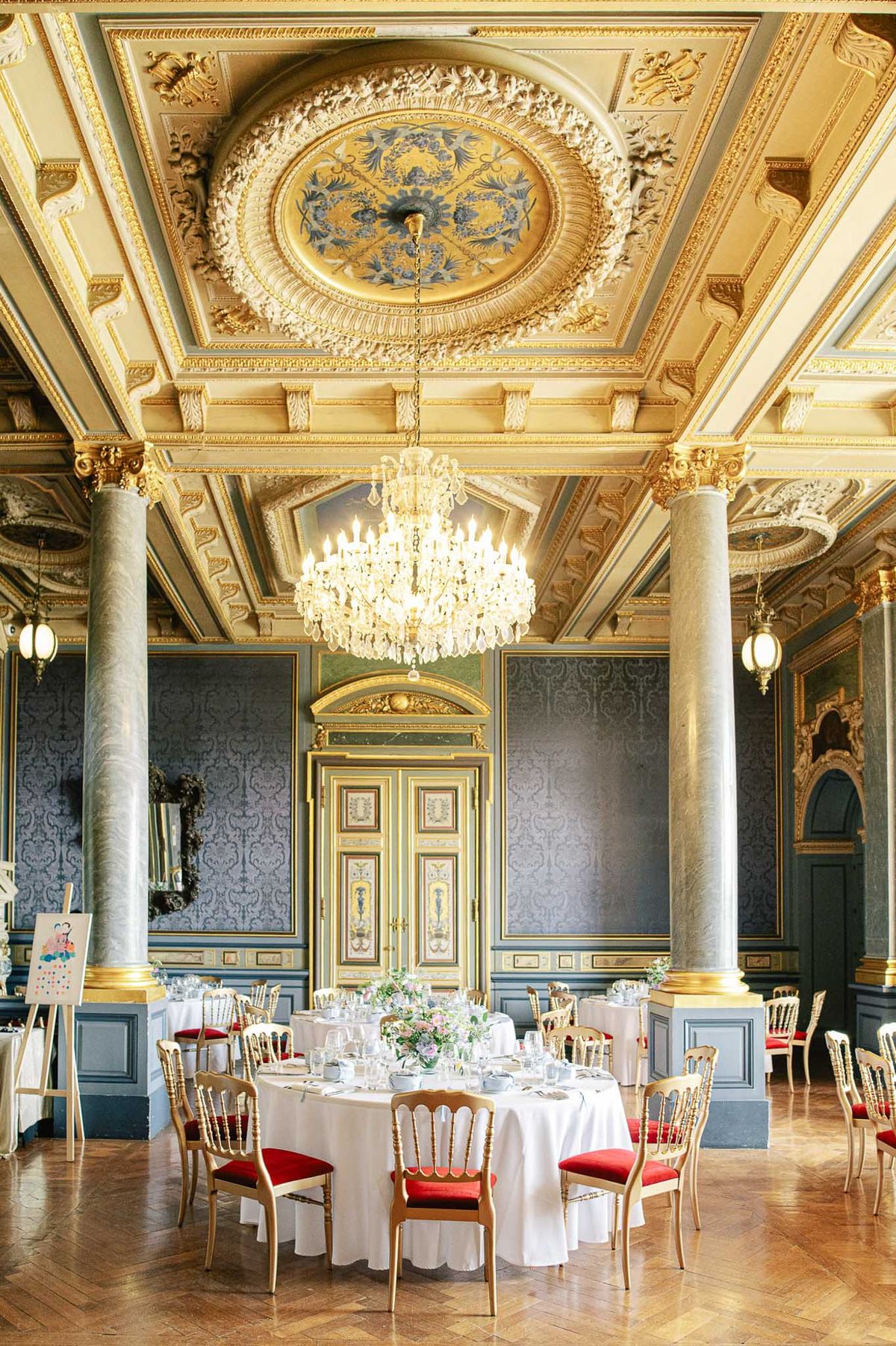Grand chateau ballroom set for wedding dinner with crystal chandelier, round tables, and pink and white floral centerpieces