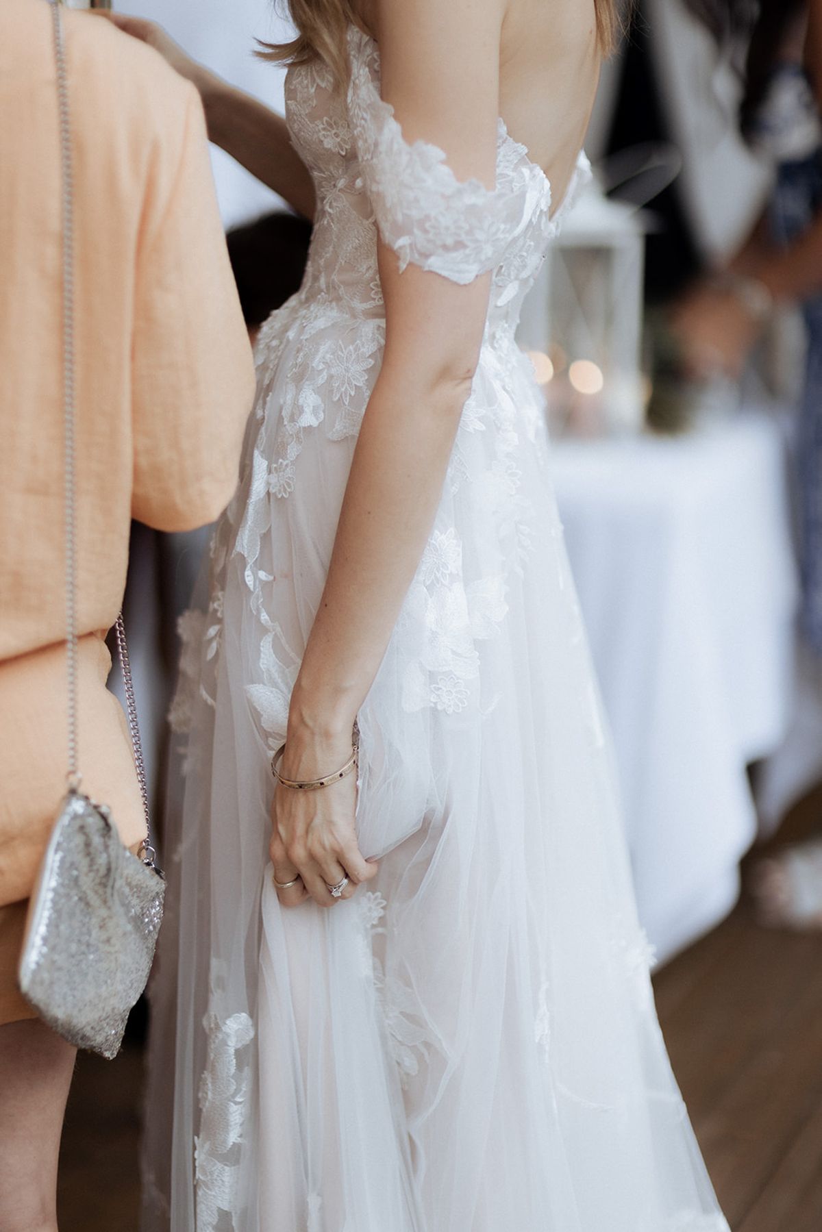 Close-up of bride in off-the-shoulder 3D floral lace tulle gown with diamond ring and gold bangle at reception