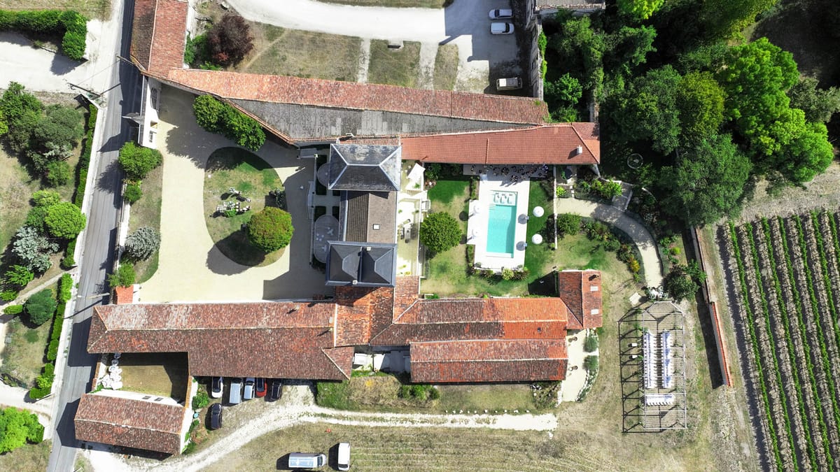 Aerial drone view of French rural estate with manor house, outbuildings, swimming pool, and vineyard rows