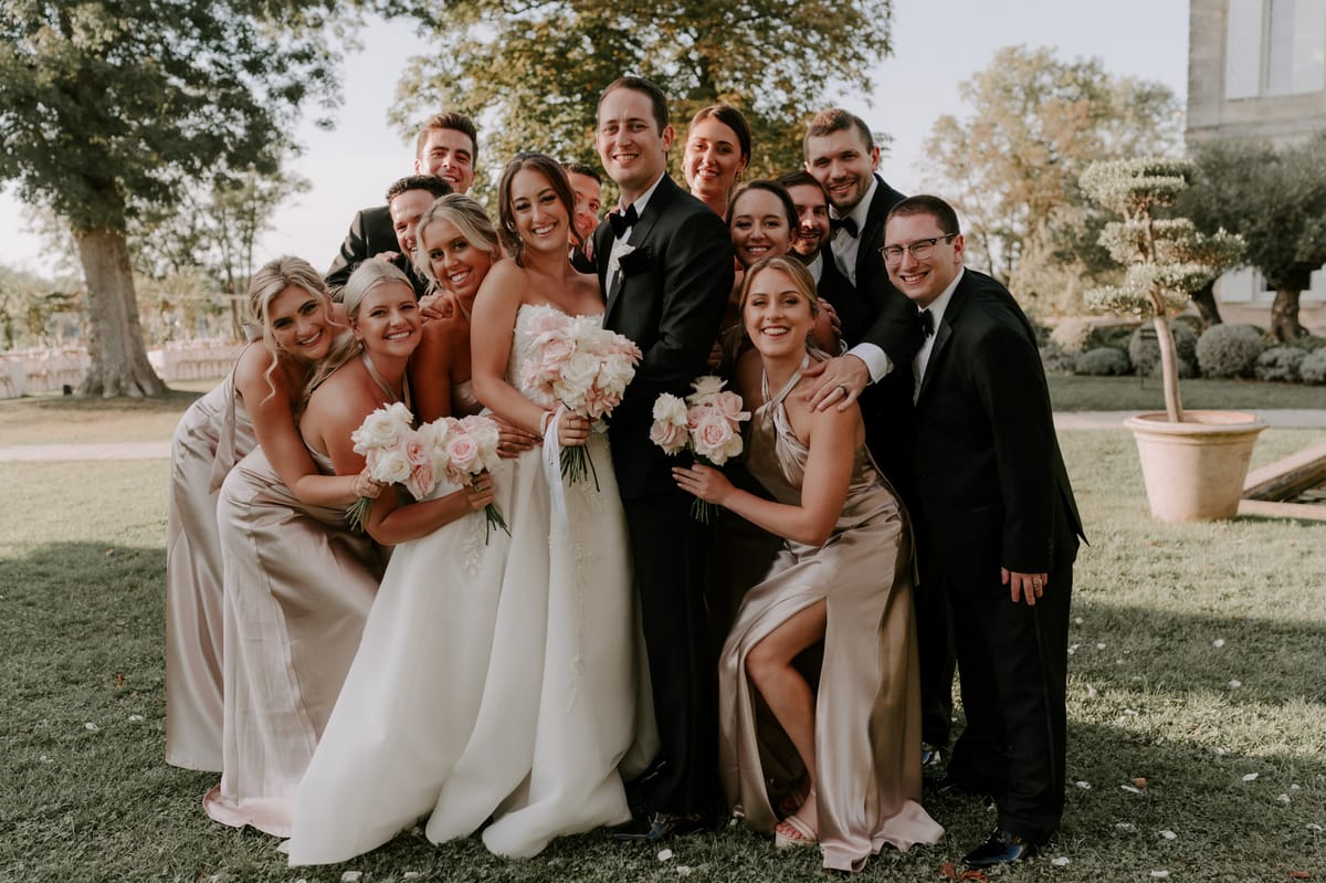 Bridal party group portrait on lawn with bridesmaids in champagne-gold gowns and groomsmen in black tuxedos