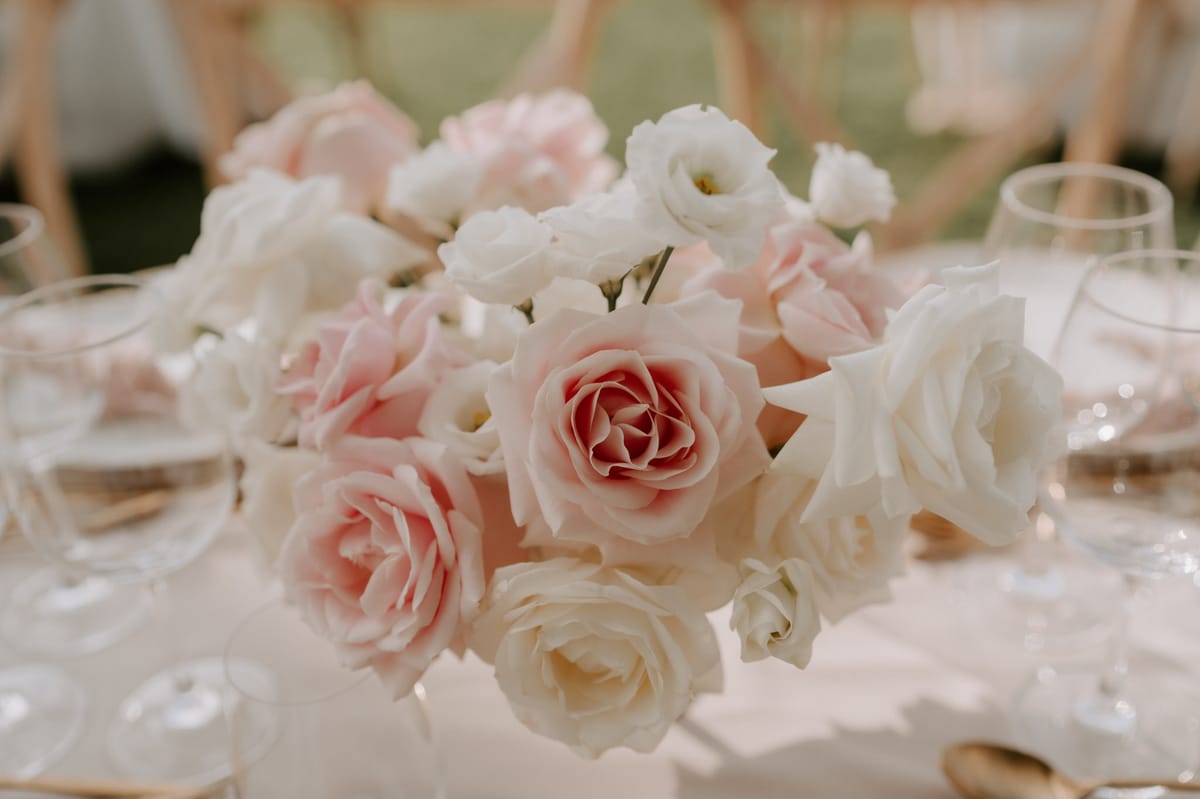 Low centerpiece of blush and ivory roses with gold-rimmed charger plates and crossback chairs