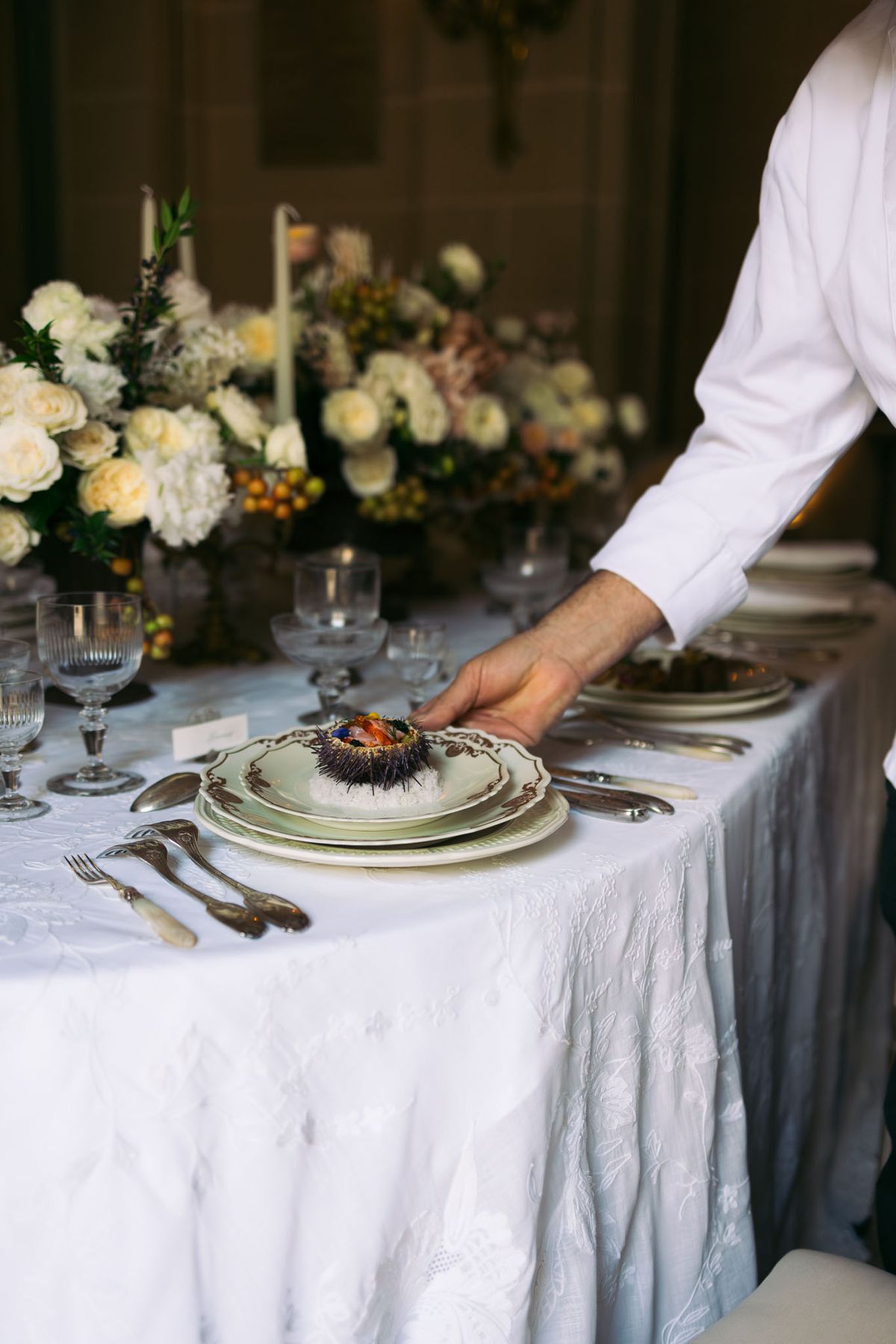 Server placing sea urchin on sage green plates with ivory rose and kumquat centerpiece bone-handled cutlery and crystal gl...