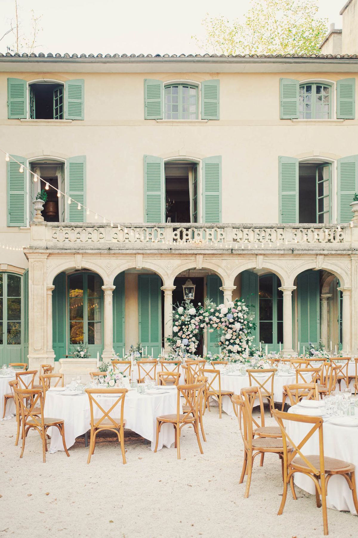 Outdoor wedding reception in French manor courtyard with round tables, white linens, and pastel floral centerpieces