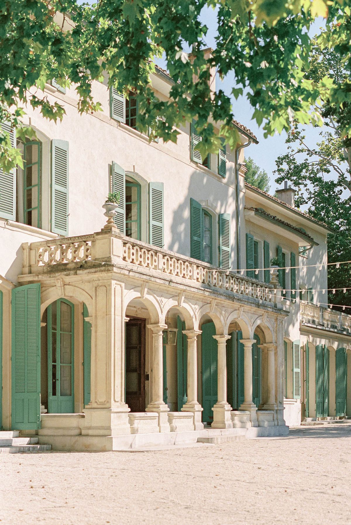 Provencal bastide with stone colonnades, teal shutters, and festoon lights on upper terrace