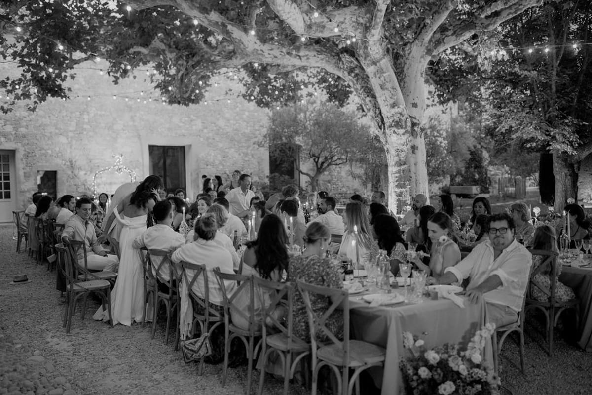 Black and white courtyard dinner under plane trees with fairy lights and cross-back chairs