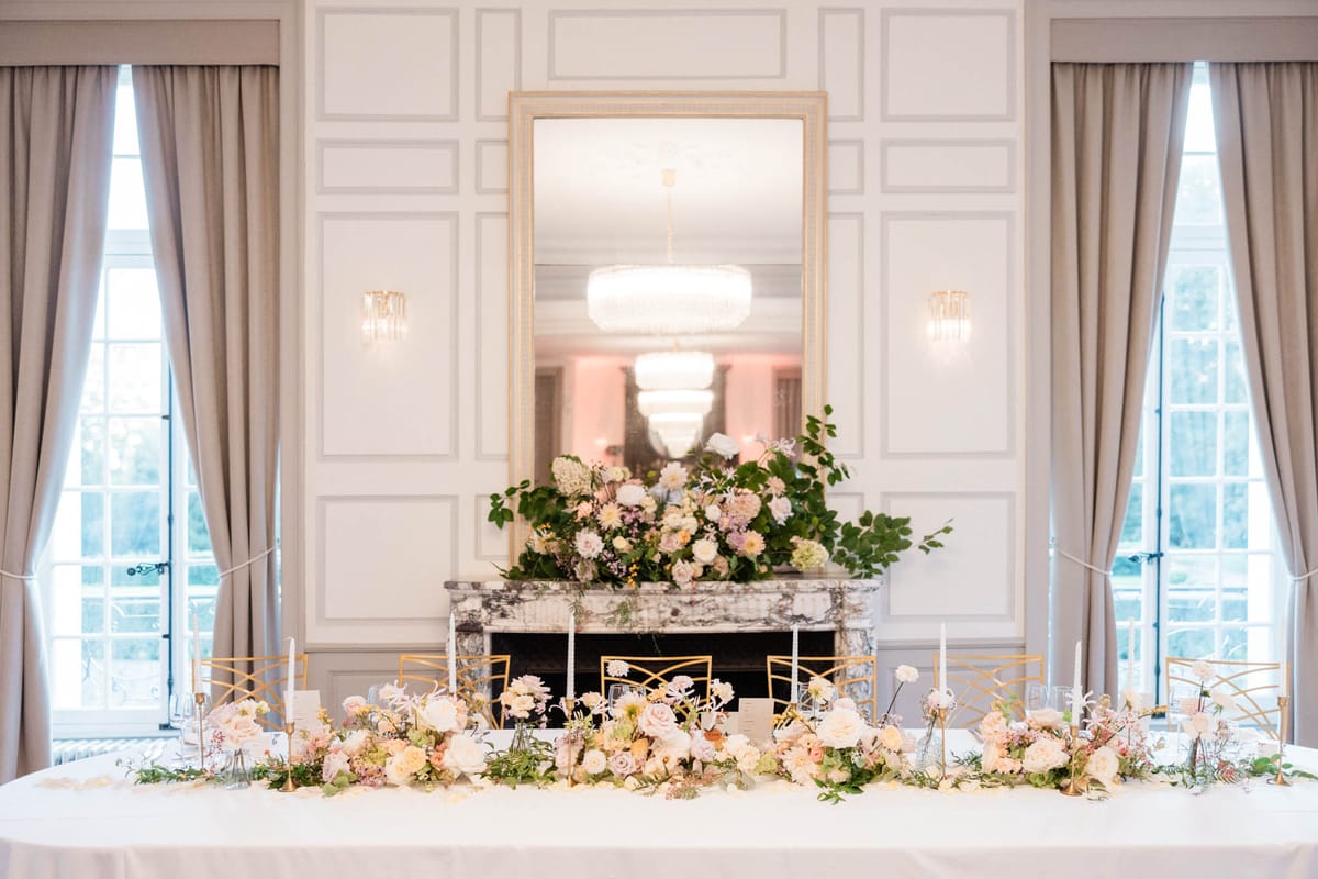 Head table with blush rose runner and gold tapers before fireplace mirror in white-panelled ballroom