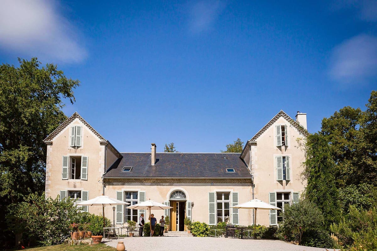 Cream-rendered French manor with sage shutters yellow doors gravel forecourt and white parasols