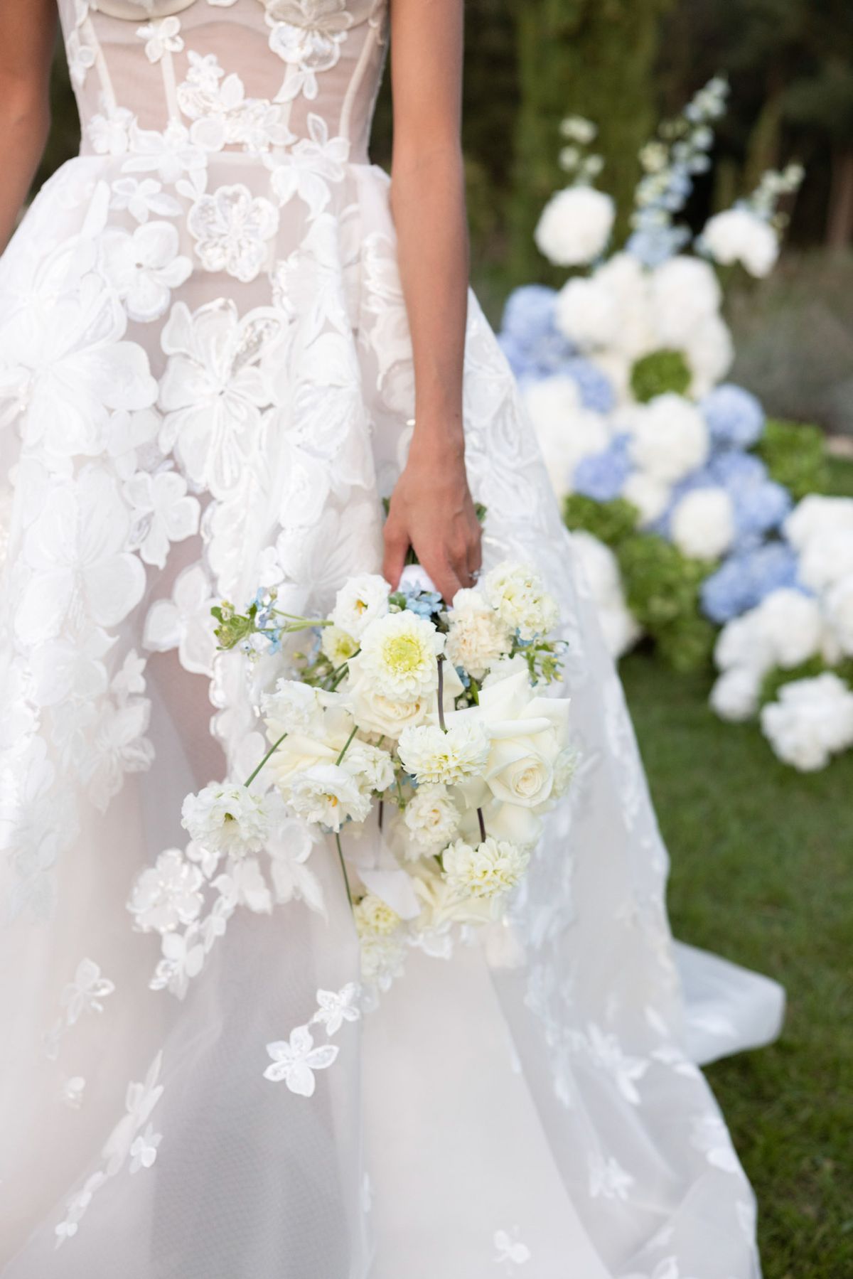 Bride holding garden-style bouquet of ivory roses, cream dahlias, and blue delphinium
